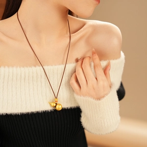 Detail of a brushed gold gourd pendant on a brown woven cord worn with a striped sweater