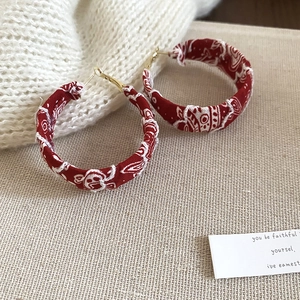 Détail de créoles en tissu rouge à motifs ethniques blancs sur fond en lin