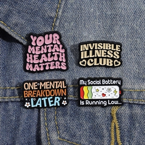 Set of four mental health enamel pins on denim jacket showing creative text and motifs