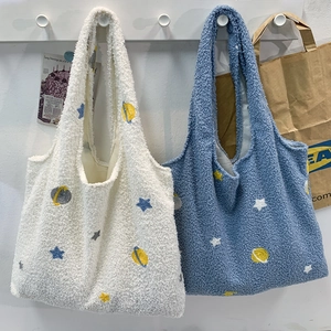 Detail of soft sherpa tote bags featuring embroidered yellow planets and colorful stars