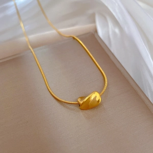 Detailed view of a gold snake chain necklace featuring a twisted bean shaped pendant