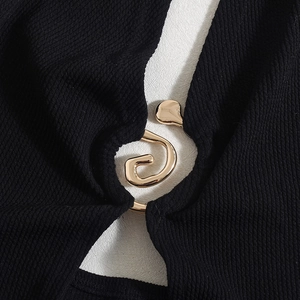 Detail einer goldenen Spiralschnalle auf schwarzem Rippstoff eines Cut-out-Kleids