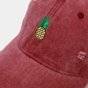Close-up of distressed wine red washed cotton baseball cap with pineapple embroidery detail