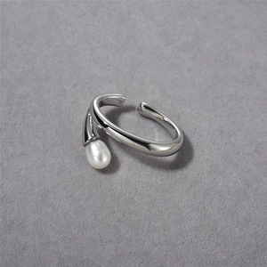 Macro detail of silver adjustable ring with a drop-shaped pearl inlay on grey surface