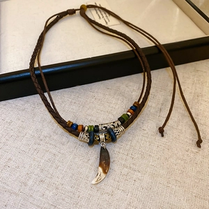 Detail of bohemian necklace with woven cord and tooth-shaped pendant on textured fabric