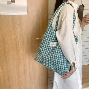 Blue and white checkered woven tote bag worn on shoulder over a white shirt