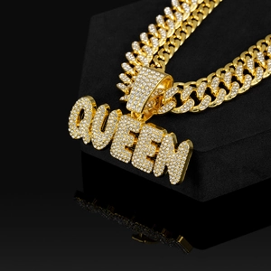 Dettaglio catena cubana dorata con ciondolo QUEEN in strass su velluto nero elegante