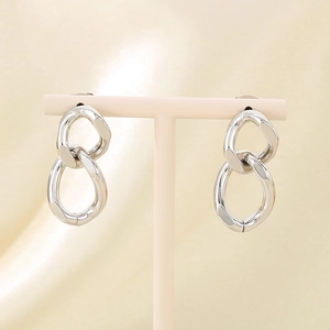 Close-up of polished silver twisted Cuban chain earrings on a pink jewelry display