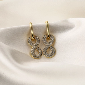 Detailed view of infinity-shaped gold earrings with clear crystals on beige silk
