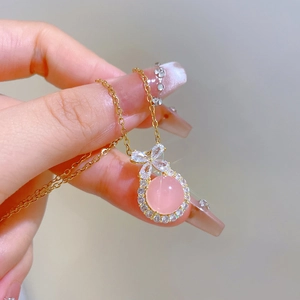 Macro view of gold-plated necklace with pink gemstone bow pendant and clear zircons