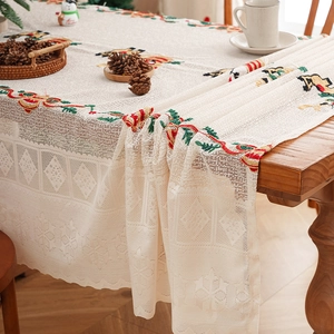 Beige Christmas lace tablecloth with snowman embroidery and wavy edges on a wooden table