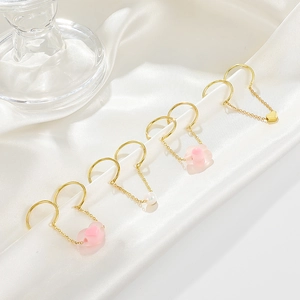 Golden jewelry set with pink hearts, flower, and pearls on white silk background