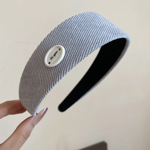 Détail de la texture du serre-tête en velours côtelé bleu avec un bouton blanc décoratif