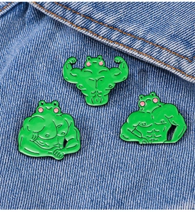 Detailed close-up of funny muscular frog enamel pins set on blue denim fabric