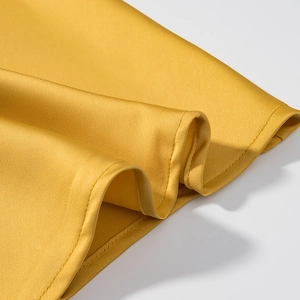Macro shot of glossy yellow satin fabric texture and precise stitching on the hem