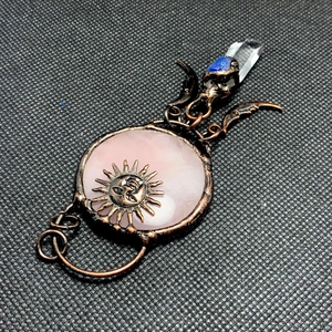 Detail of copper wire wrapped pink crystal pendant with sun face and moon design