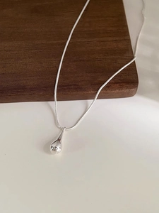 Macro shot of polished silver teardrop pendant on minimalist snake chain necklace