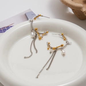 Detailed view of two-tone 18K gold and silver drop earrings with pearls on white plate
