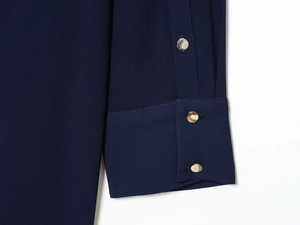 Détail d'une manche de robe bleu foncé avec trois boutons métalliques dorés décoratifs