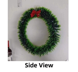 Side view of a green and black Christmas wreath with a red satin bow on a white wall
