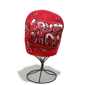 Detail of red knit hat featuring white LOVER GIRL text and cherry heart patterns
