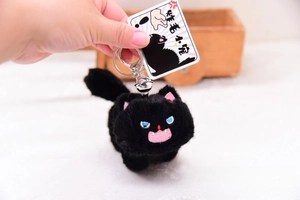 Close-up of black plush cat keychain with silver bell and illustrated brand card