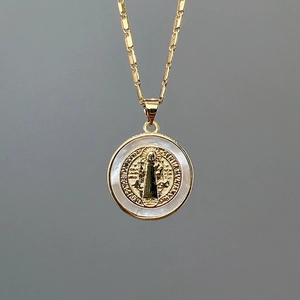 Detailed close-up of a gold-plated Saint Benedict medal with white mother-of-pearl inlay
