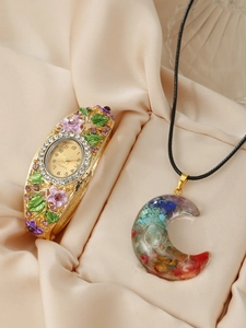 Macro view of gold floral enamel watch and moon crescent gemstone pendant set on silk