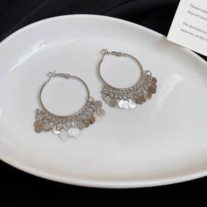 Detailed shot of silver metal hoop earrings with round sequin tassels on a ceramic plate