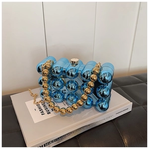 Detail view of blue acrylic capsule bag with gold ball handle and chain strap on a book