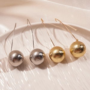 Minimalist gold and silver brushed metal sphere earrings on a white ceramic plate