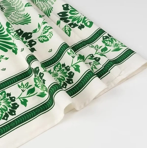 Detailed close-up of white fabric with green botanical prints and fine stitching