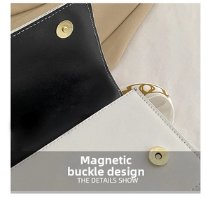Close-up of golden magnetic snap closure on a black and white leather handbag