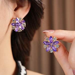 Dettaglio di orecchini a fiore vintage dorati con cristalli viola e punti luce