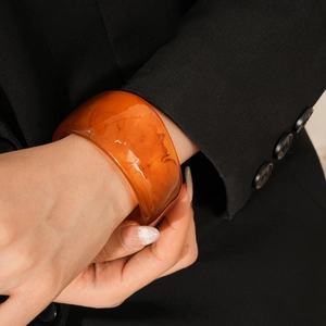 Detail of amber resin bangle with swirling texture worn over a black blazer sleeve