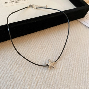 Detail of silver starfish pendant with textured metallic finish on black cord necklace