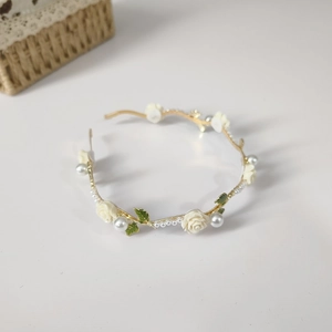 Detail of golden headband with white roses, green leaves and pearls on white background