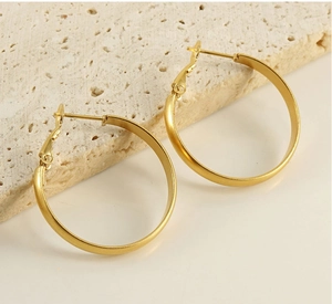 Close-up of matte gold stainless steel hoop earrings on a textured beige stone base