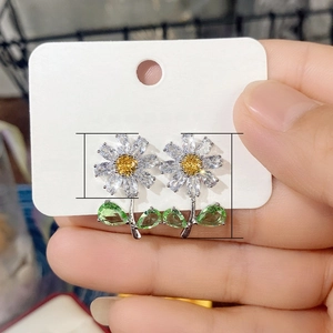 Daisy flower earrings with yellow crystal core and green leaf charms on hand-held card