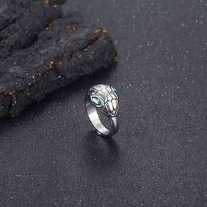Macro shot of punk style snake ring with green gem eyes on dark charcoal wood background