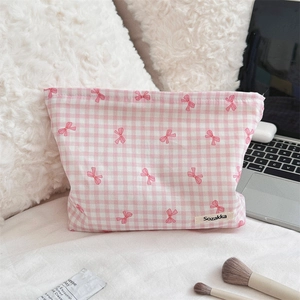Pink checkered toiletry bag with cute bow pattern and side brand label detail on bed