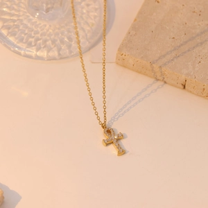 Golden Ankh cross necklace with sparkling zircon pavé on an elegant stone surface