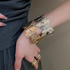 Macro detail of gold butterfly cuff bracelet with textured hollow wings and metallic finish