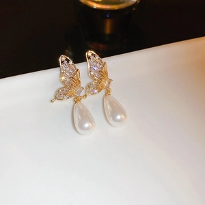 Macro shot of gold-plated butterfly earrings with zircons and drop pearl charms