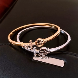 Close-up of 18K gold and silver plated arrow cross bangles with peace sign and white zircons