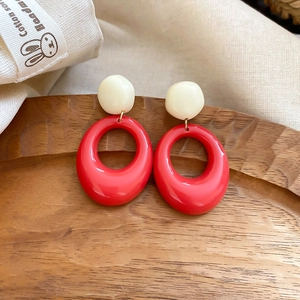 Detailed macro view of resin drop earrings with red rings on a textured wooden tray