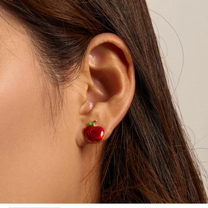 Close-up of a person wearing a red apple stud earring with gold edges and fine glitter