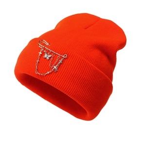 Detailed view of bright orange knit beanie with metal chain and butterfly pendant decoration