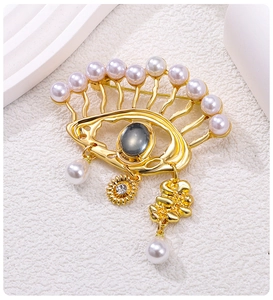 Close-up of golden Evil Eye brooch with pearls and charms on white pedestal