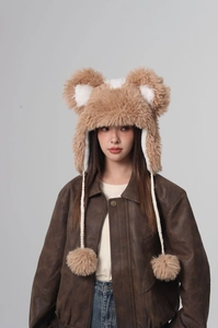 Detail of plush brown bear ear hat with white braided drawstrings and fluffy pom-poms